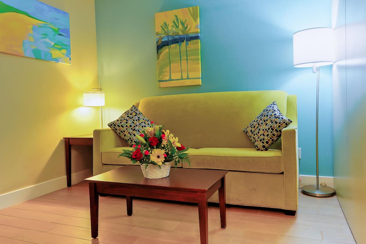 A room with a sofa, a coffee table with a flower arrangement, a lamp, and artwork on the walls.