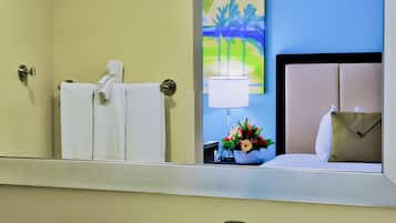 A hotel bathroom with a large mirror, a sink, a towel rack, a painting, and a flower arrangement.