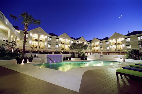 A hotel pool area with a crescent moon in the sky, surrounded by multi-story buildings with balconies.