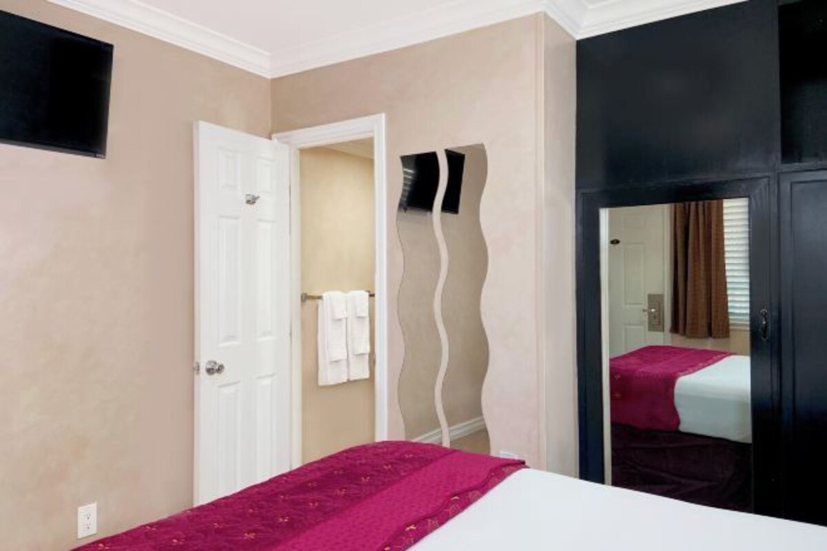 A hotel room with a bed, a white door, a mirror, and a wall with a wavy design.