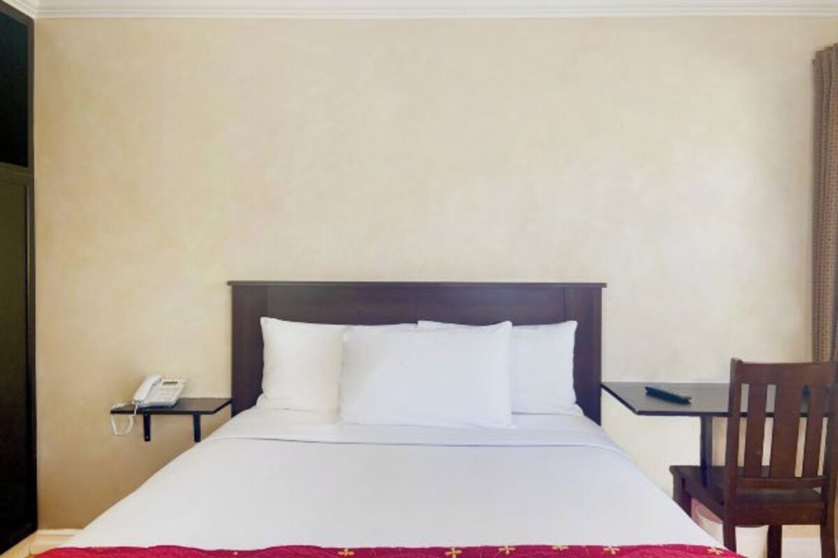 Habitación de hotel con cama, mesita de noche con teléfono, una silla y una pequeña mesa.