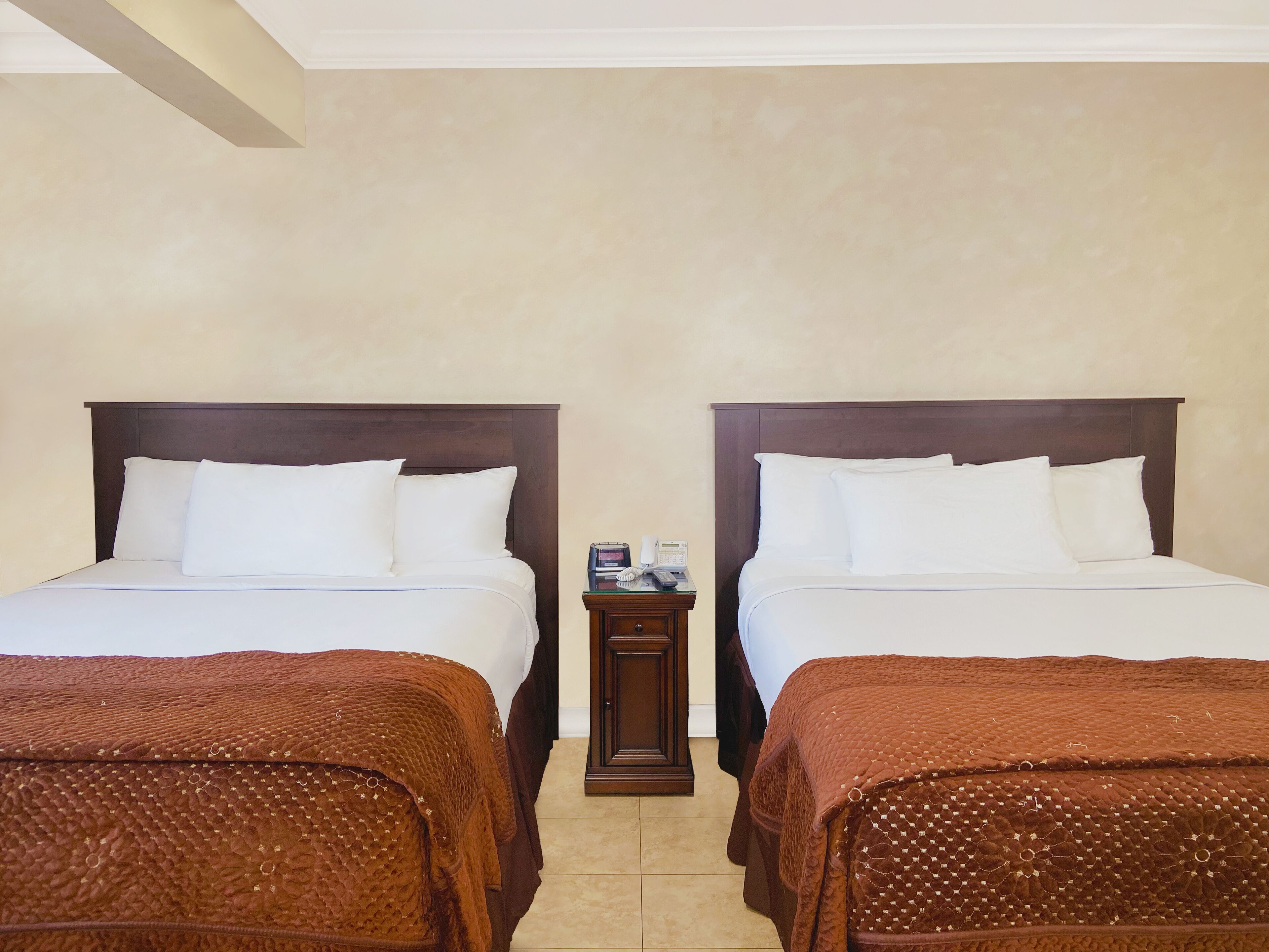 A hotel room with two beds, a nightstand with a phone, and a brown textured blanket.