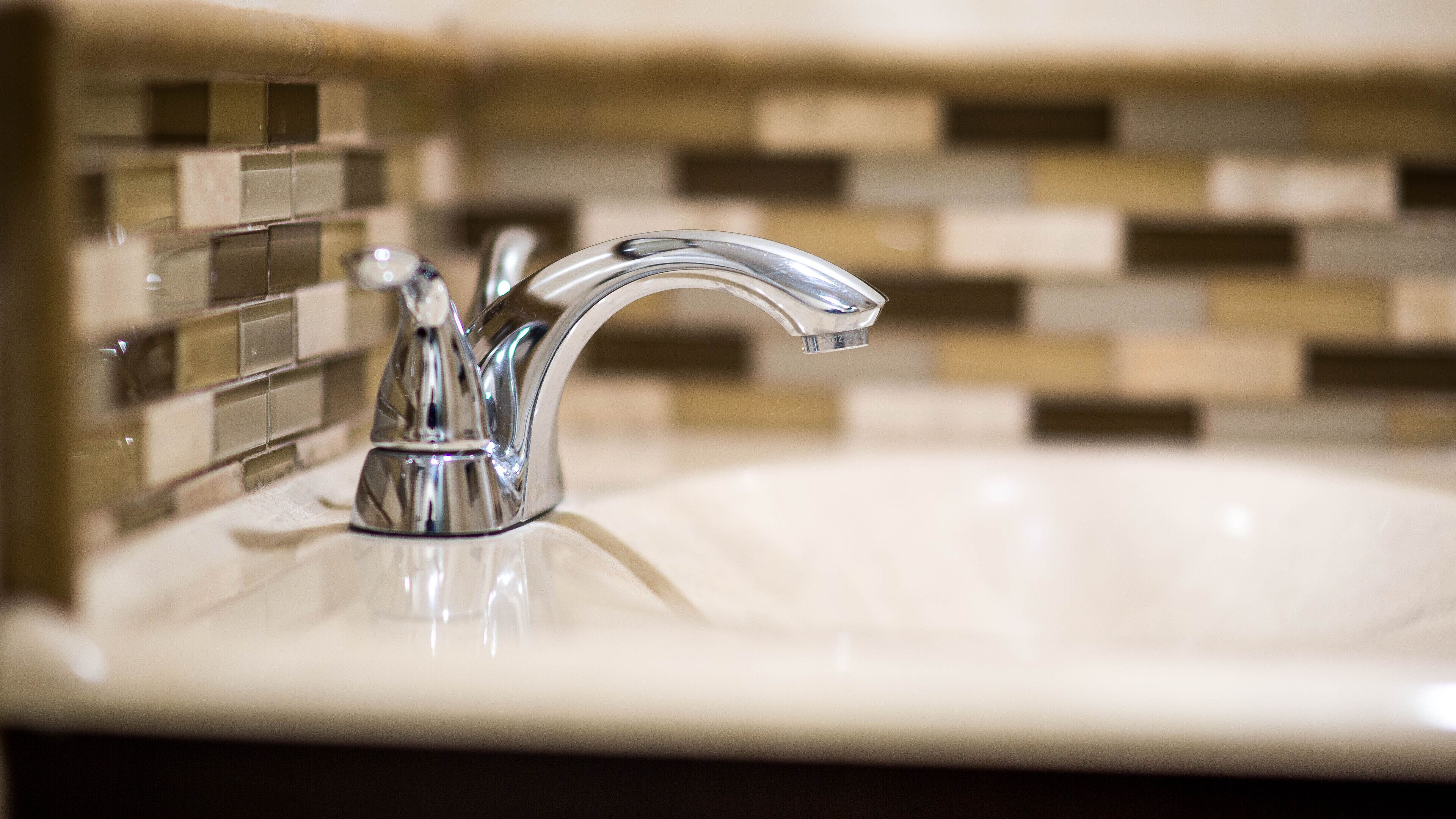 A bathroom sink with a chrome faucet and a tiled backsplash.