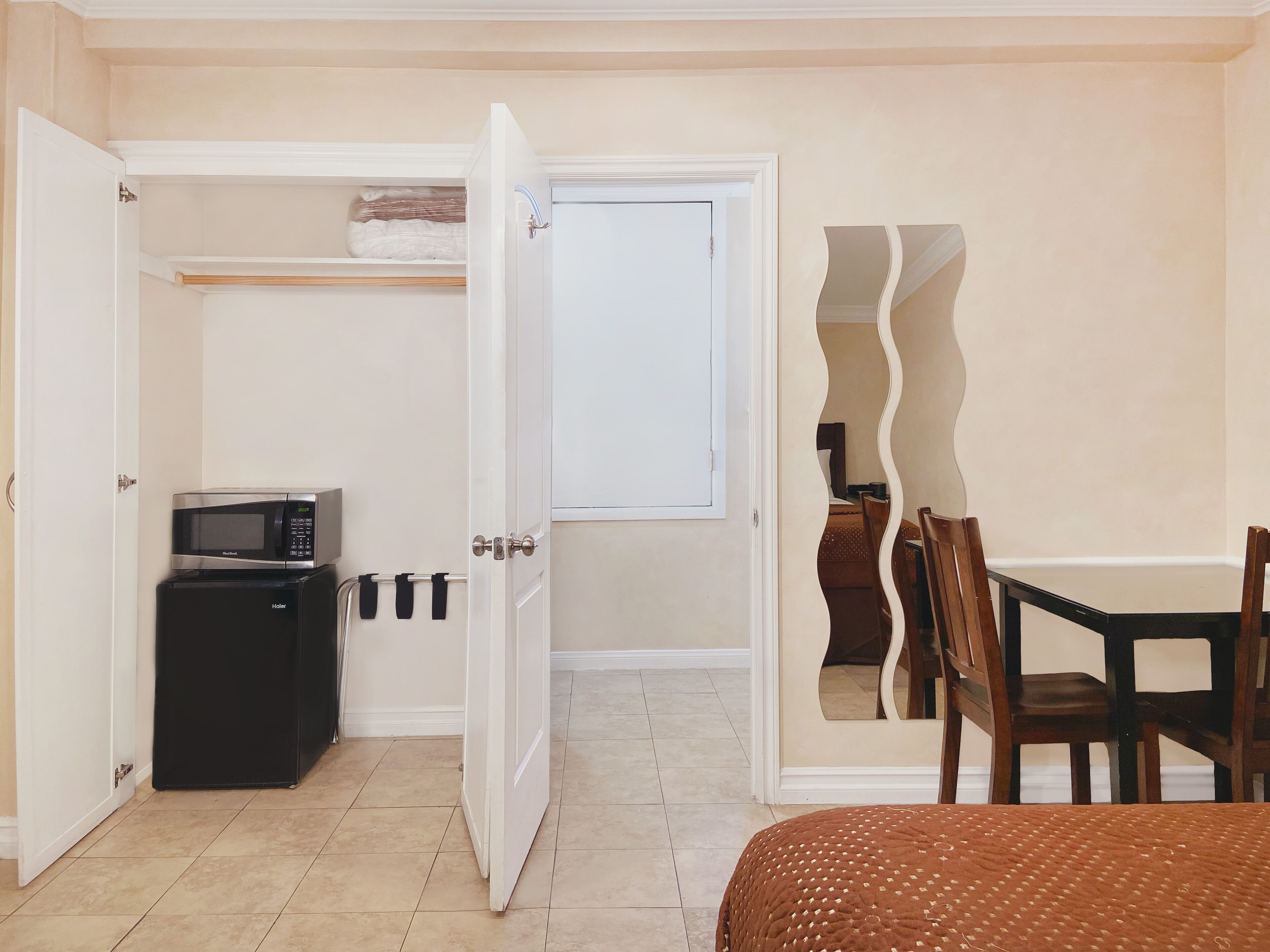 Una camera d'albergo con angolo cottura, un'area pranzo con tavolo e sedie, e un letto con copripiumino a fantasia marrone.