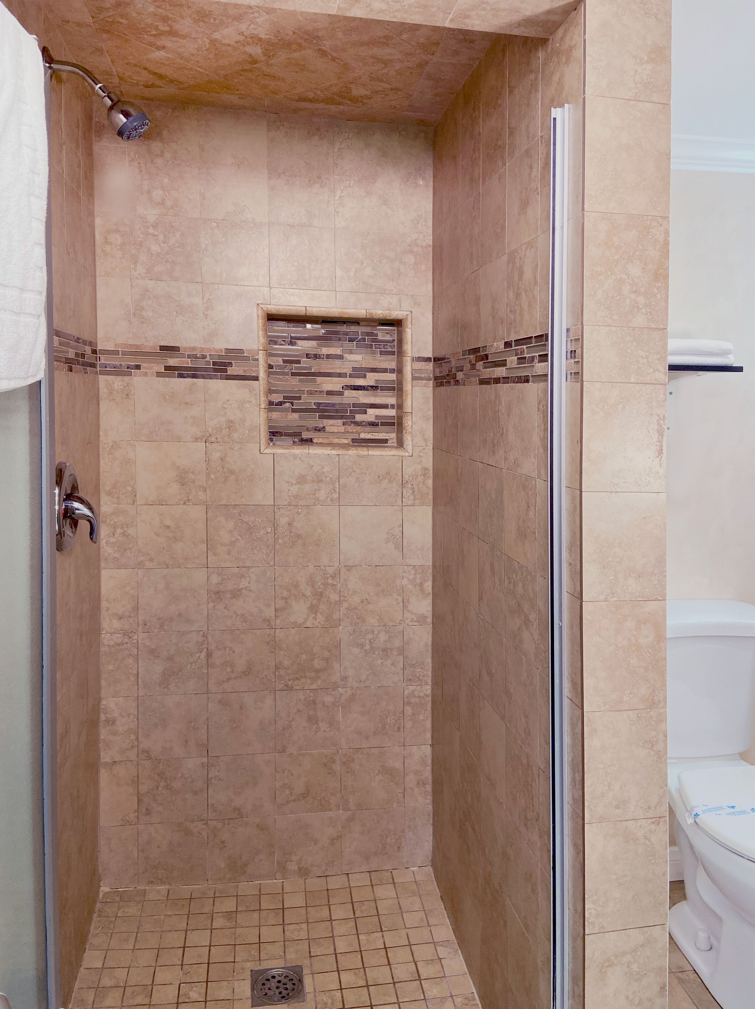 A walk-in shower with beige tiles, a glass door, and a small decorative tile feature on the wall.