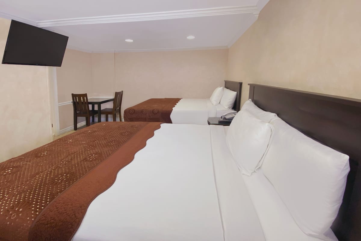 A hotel room with two beds, a small table, and a TV mounted on the wall.