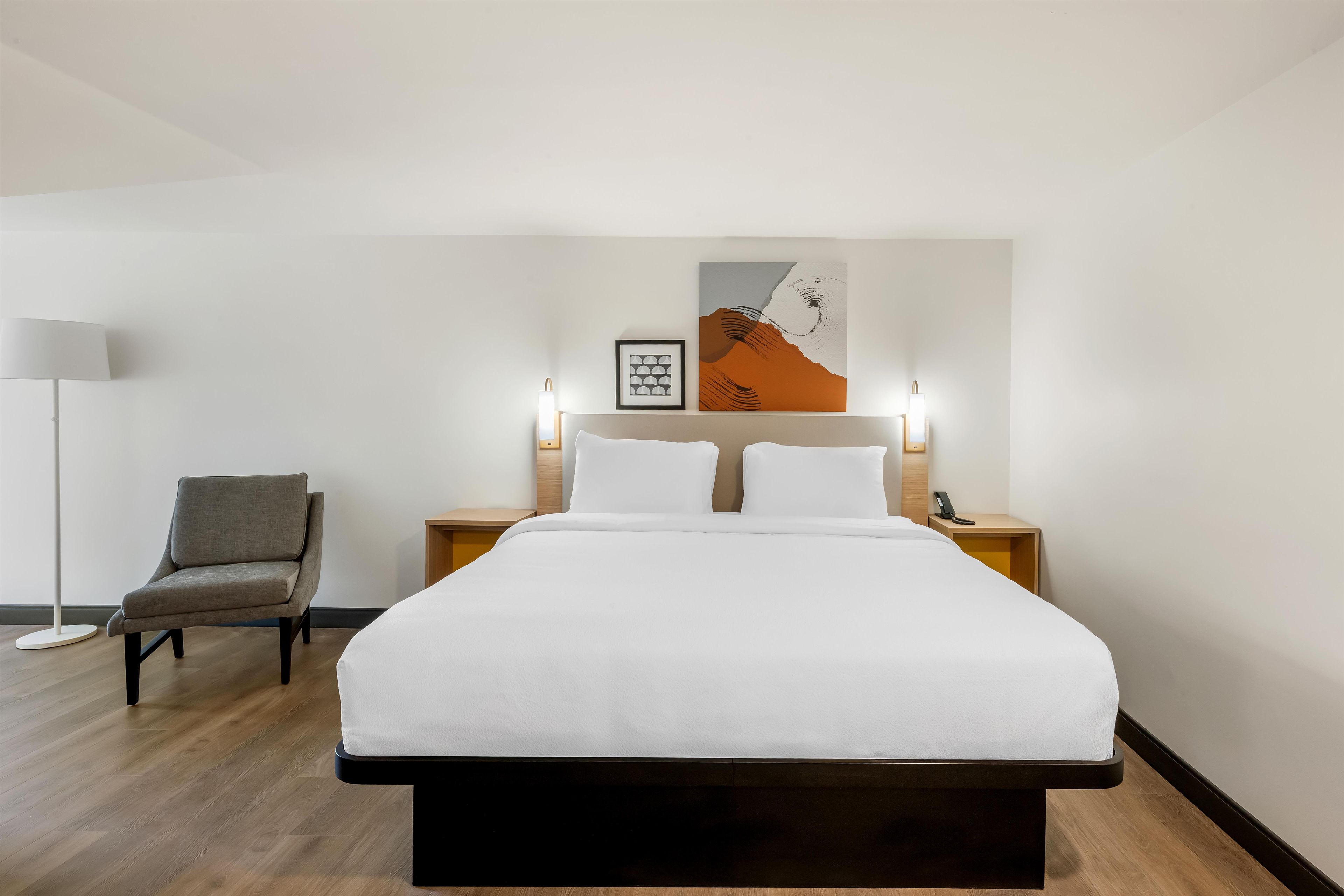 Ein Hotelzimmer mit einem Bett, einem Sessel, einem Nachttisch mit Lampe und einem an der Wand befestigten Telefon.