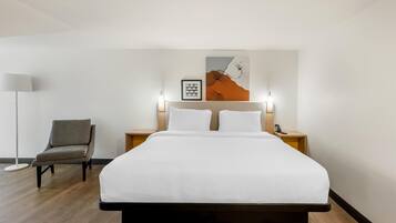 Ein Hotelzimmer mit einem Bett, einem Sessel, einem Nachttisch mit Lampe und einem an der Wand befestigten Telefon.