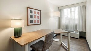 Una habitación de hotel con escritorio, silla, dos lámparas, ventana con cortinas y radiador.