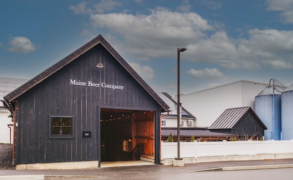 A wooden building with a sign reading "Maine Beer Company" and an open door.