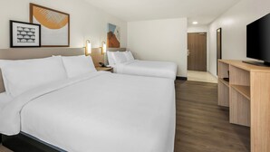 Habitación de hotel con dos camas, un televisor, un escritorio y obras de arte en las paredes.