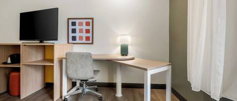 A hotel room with a desk, chair, television, and a lamp.