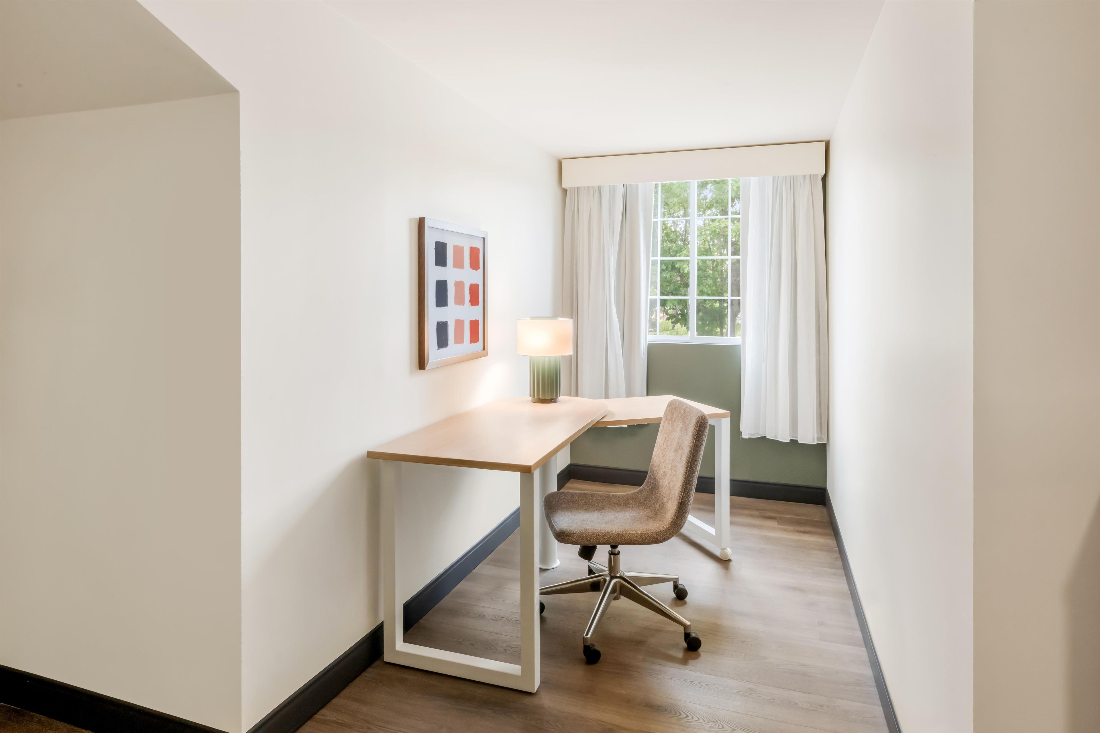 A room with a desk, chair, lamp, and a window with curtains.
