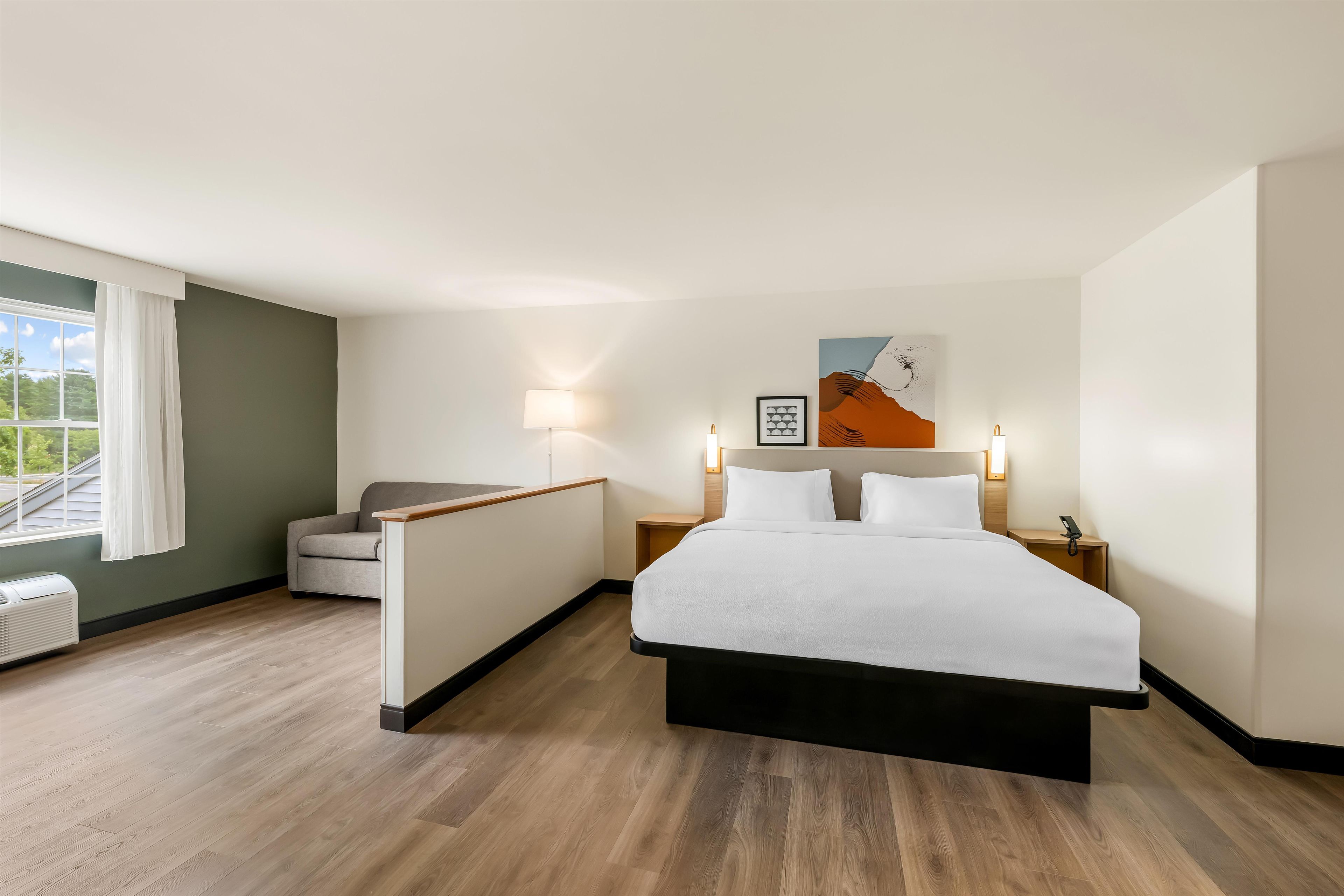 A hotel room with a bed, a sofa, a desk, and a window with curtains.