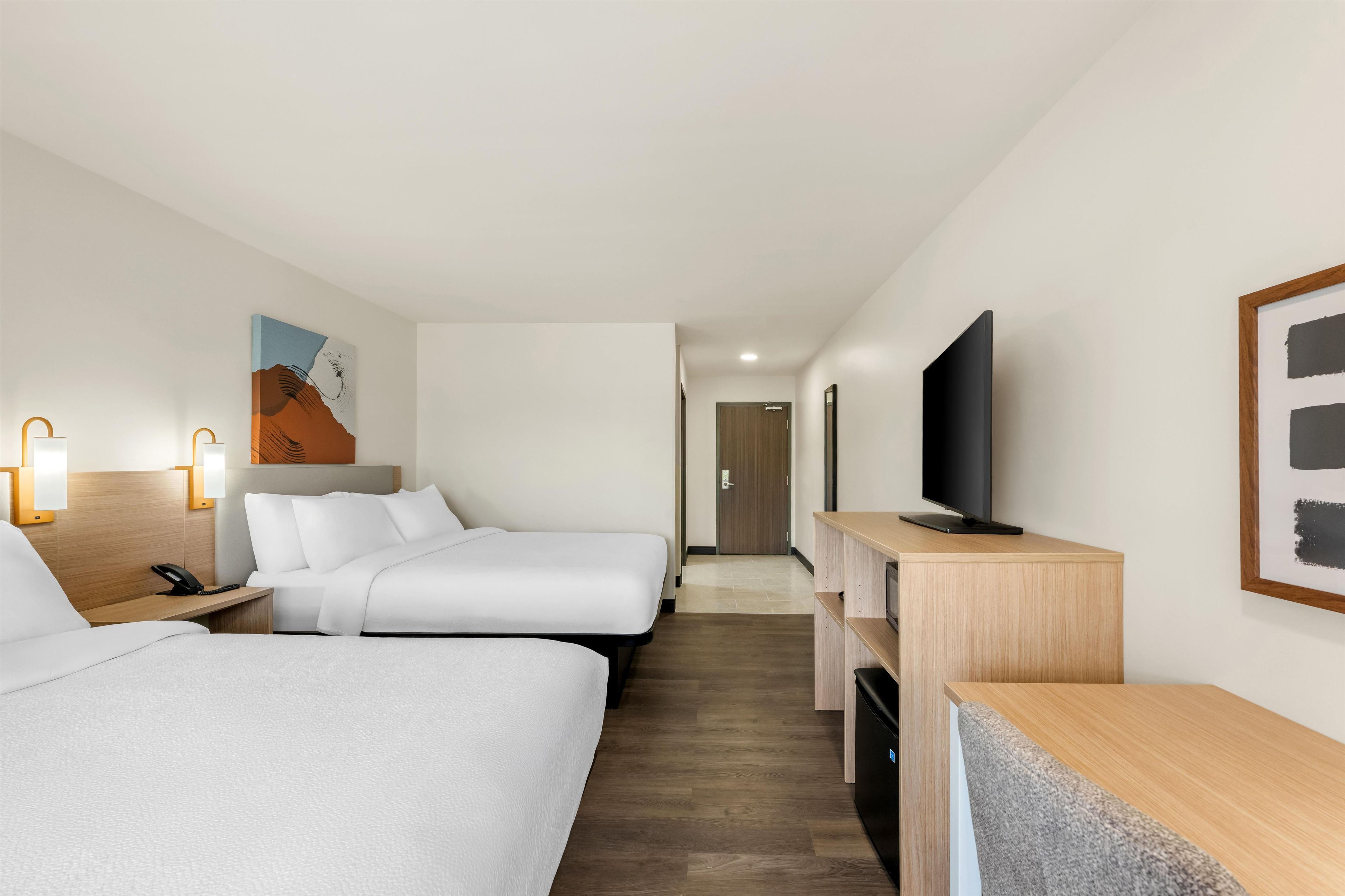 Habitación de hotel con dos camas, un escritorio, un televisor y obras de arte en las paredes.
