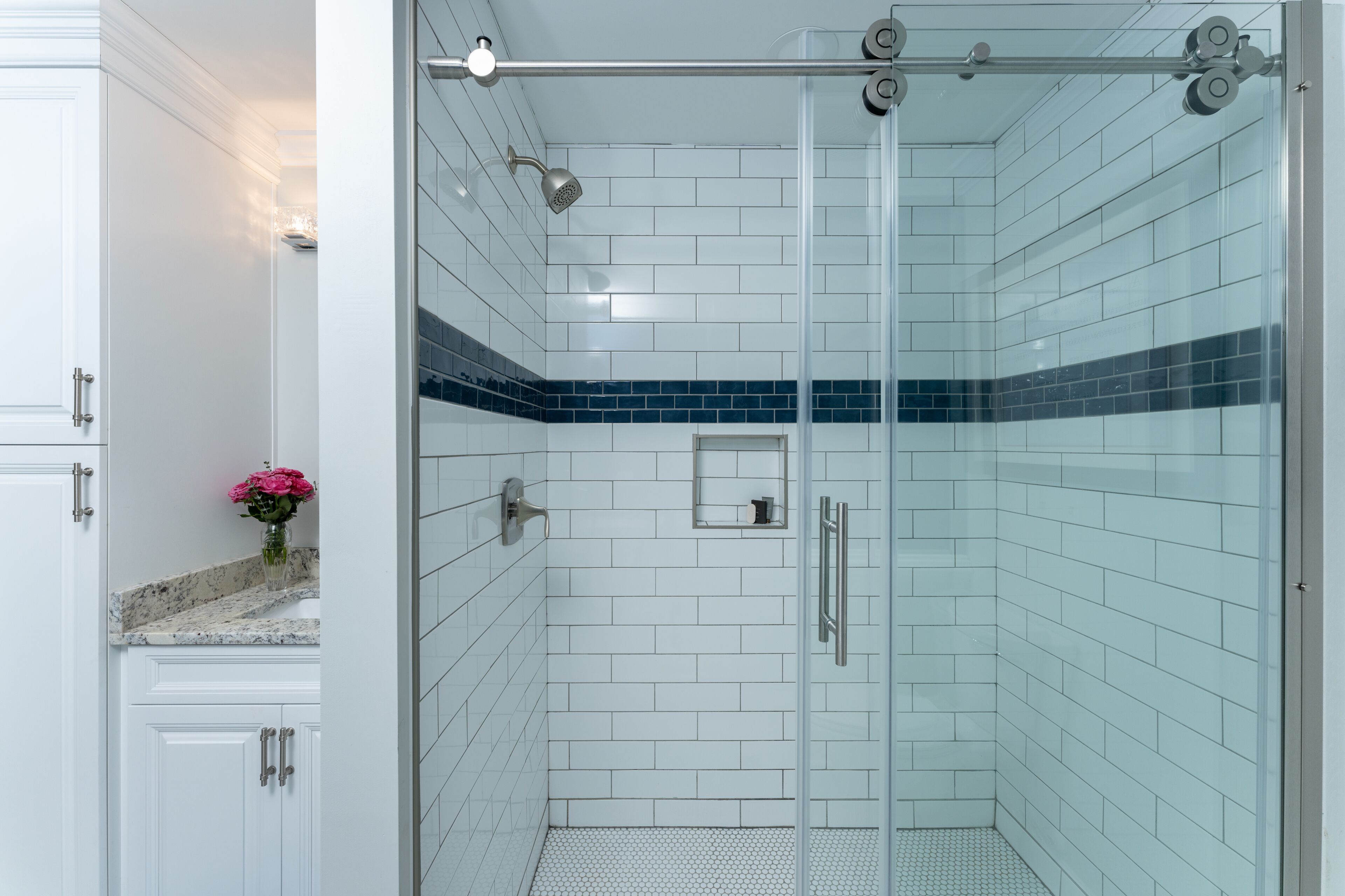 A modern bathroom with white subway tiles, a glass shower enclosure, and a small vanity with a pink flower vase.