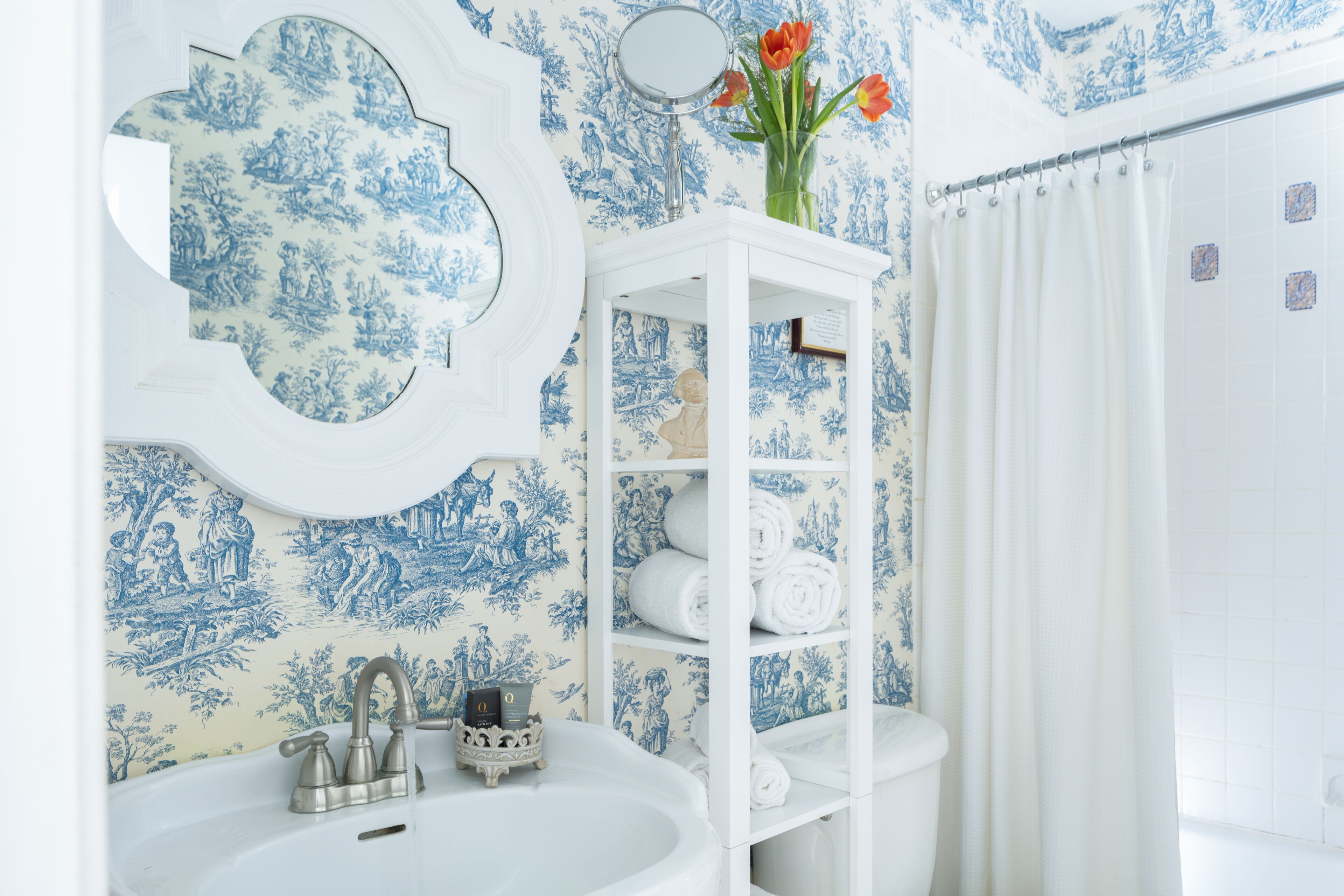 A bathroom with a sink, mirror, and a white shelf with towels.