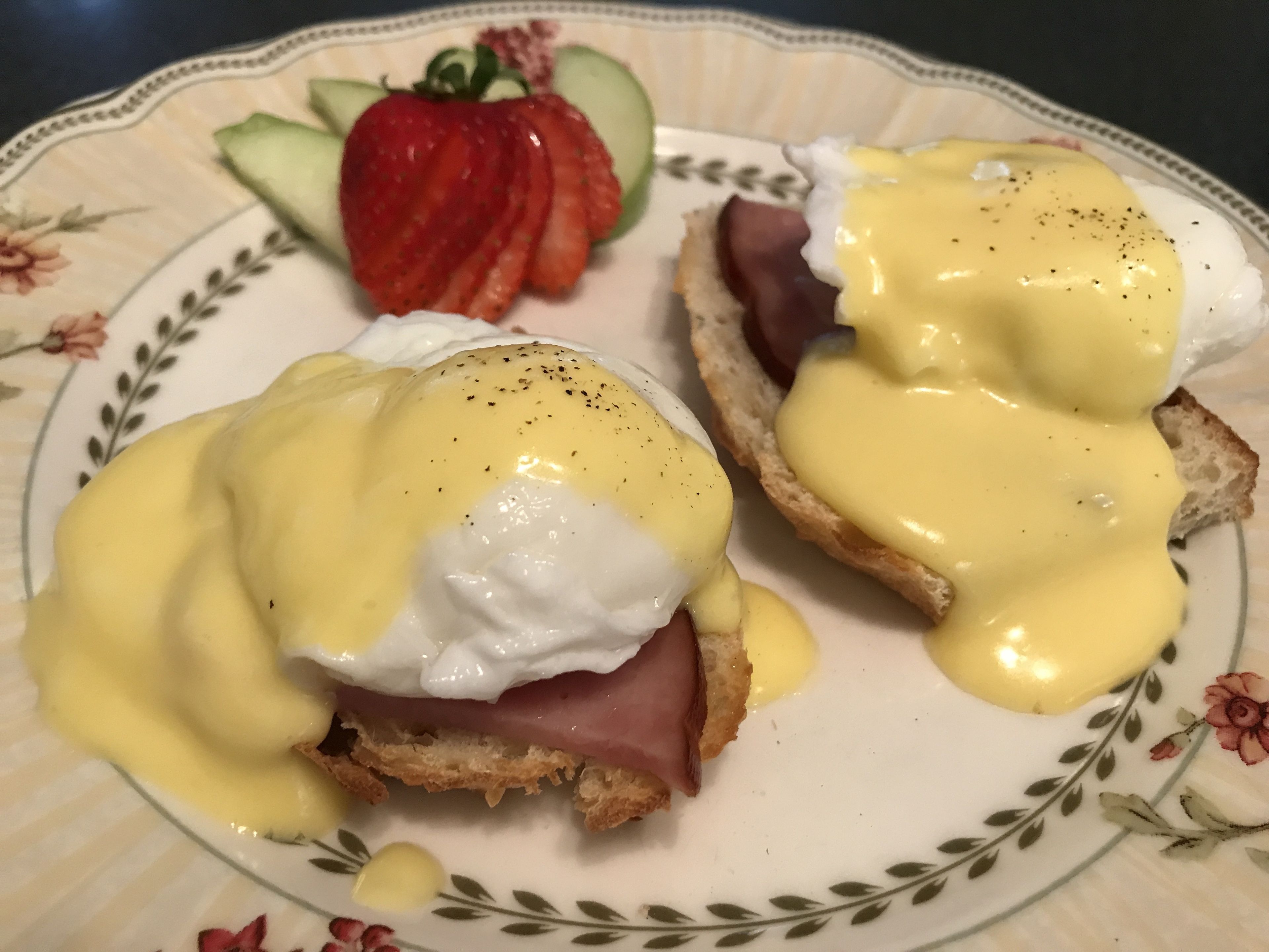 En tallrik med två ägg Benedict-smörgåsar, skinka och en jordgubbe.