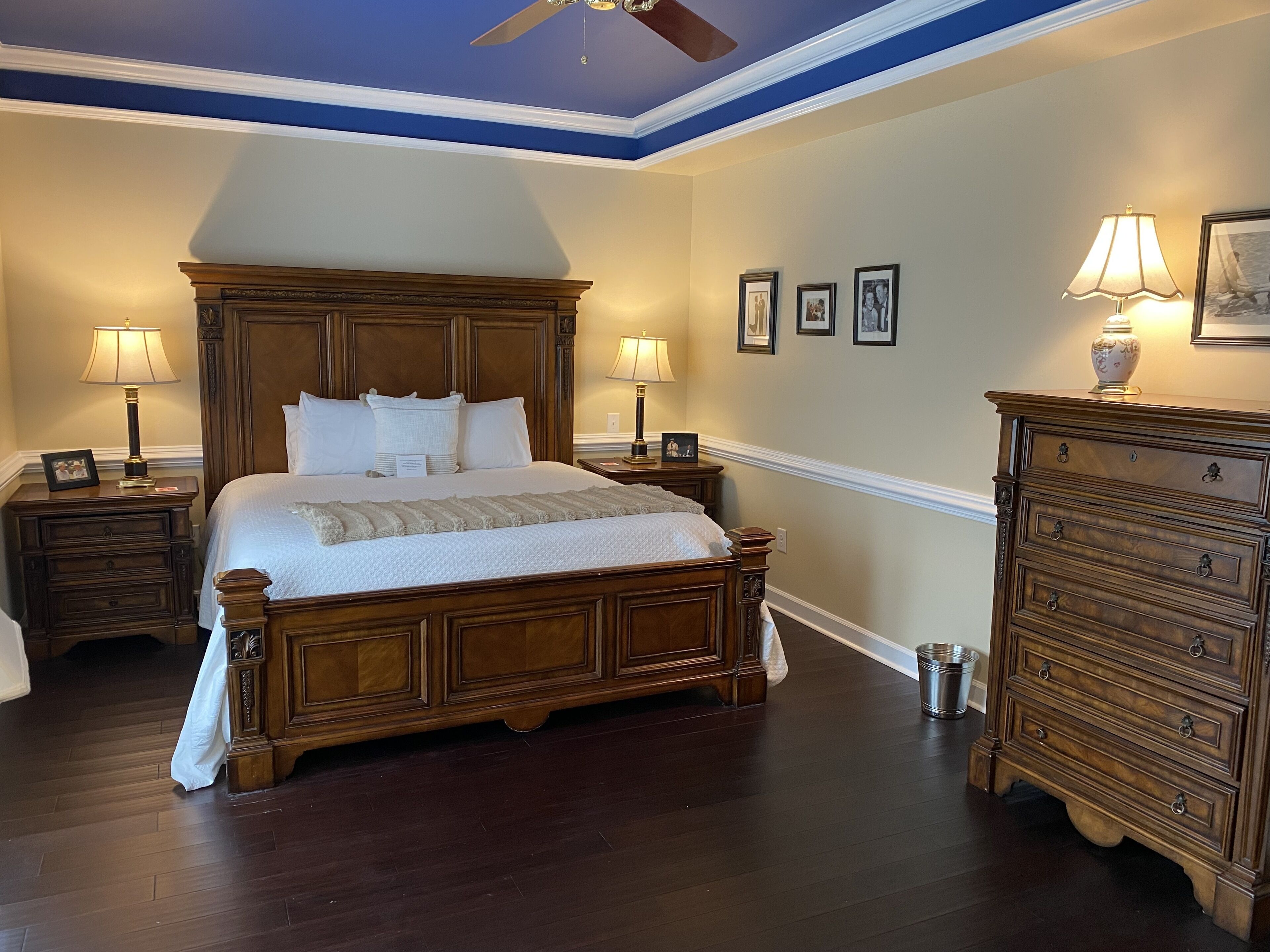 Un dormitorio con una cama de madera grande, dos mesitas de noche con lámparas, un aparador y cuadros enmarcados en la pared.