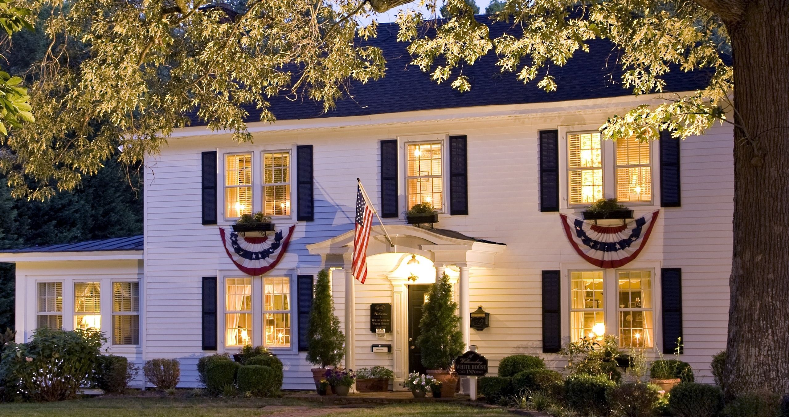 Ein weißes Gebäude mit dunklen Fensterläden, eine amerikanische Flagge und ein Schild mit der Aufschrift 'White House Inn'.