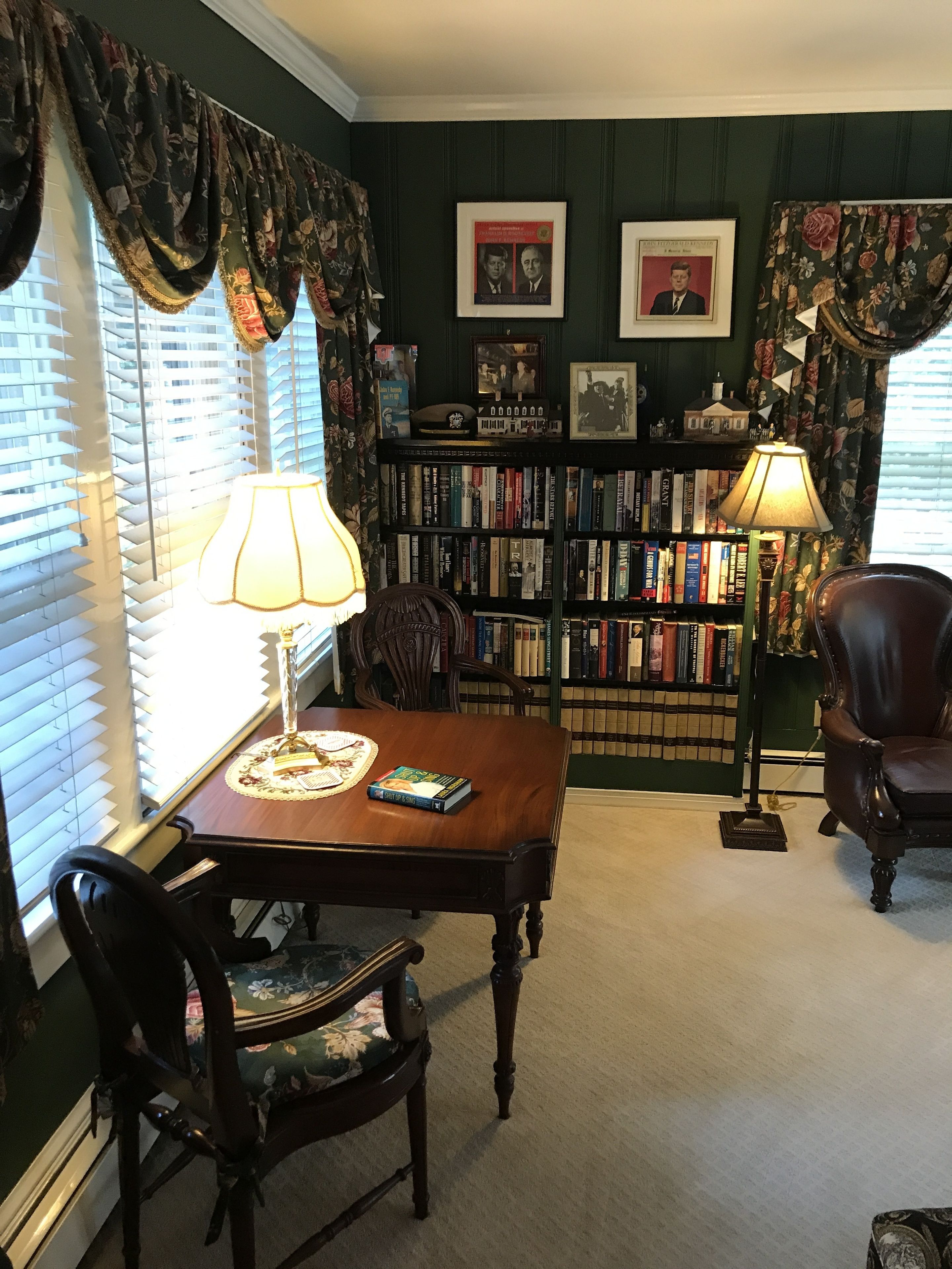 A room with a wooden table, two chairs, a bookshelf, and a lamp.