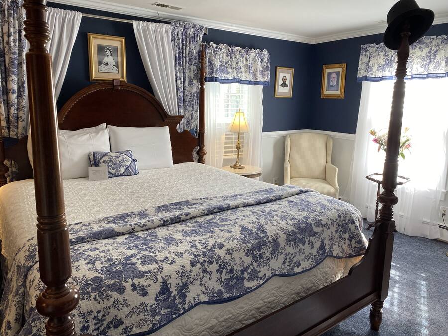 Un letto a baldacchino con copriletto floreale, un comodino con lampada, una sedia e quadri appesi al muro.
