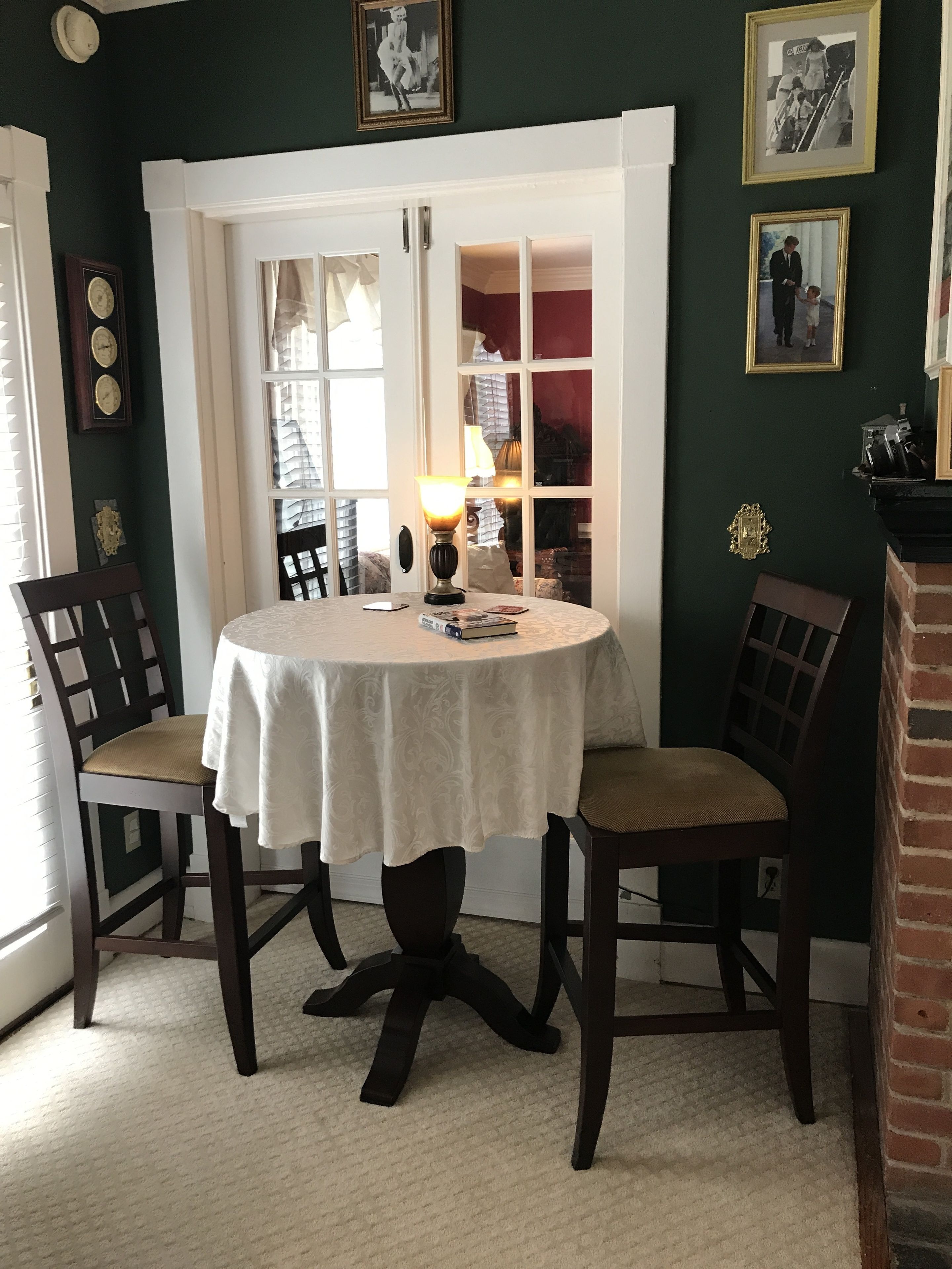 Un comedor con una mesa redonda, dos sillas, una lámpara y una estantería al fondo.