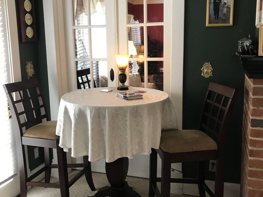 Un comedor con una mesa redonda, dos sillas, una lámpara y una estantería al fondo.