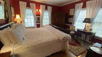 A bedroom with a large bed, a wooden wardrobe, a desk with a lamp, and a chair.