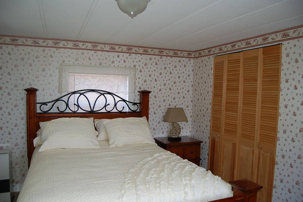 A bedroom with a wooden bed, a nightstand, a lamp, a window, and a wooden wardrobe.