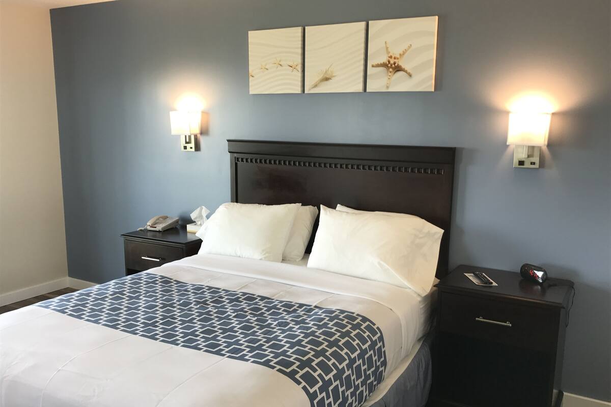 A hotel room with a large bed, two bedside tables, a nightstand, and wall-mounted lamps.