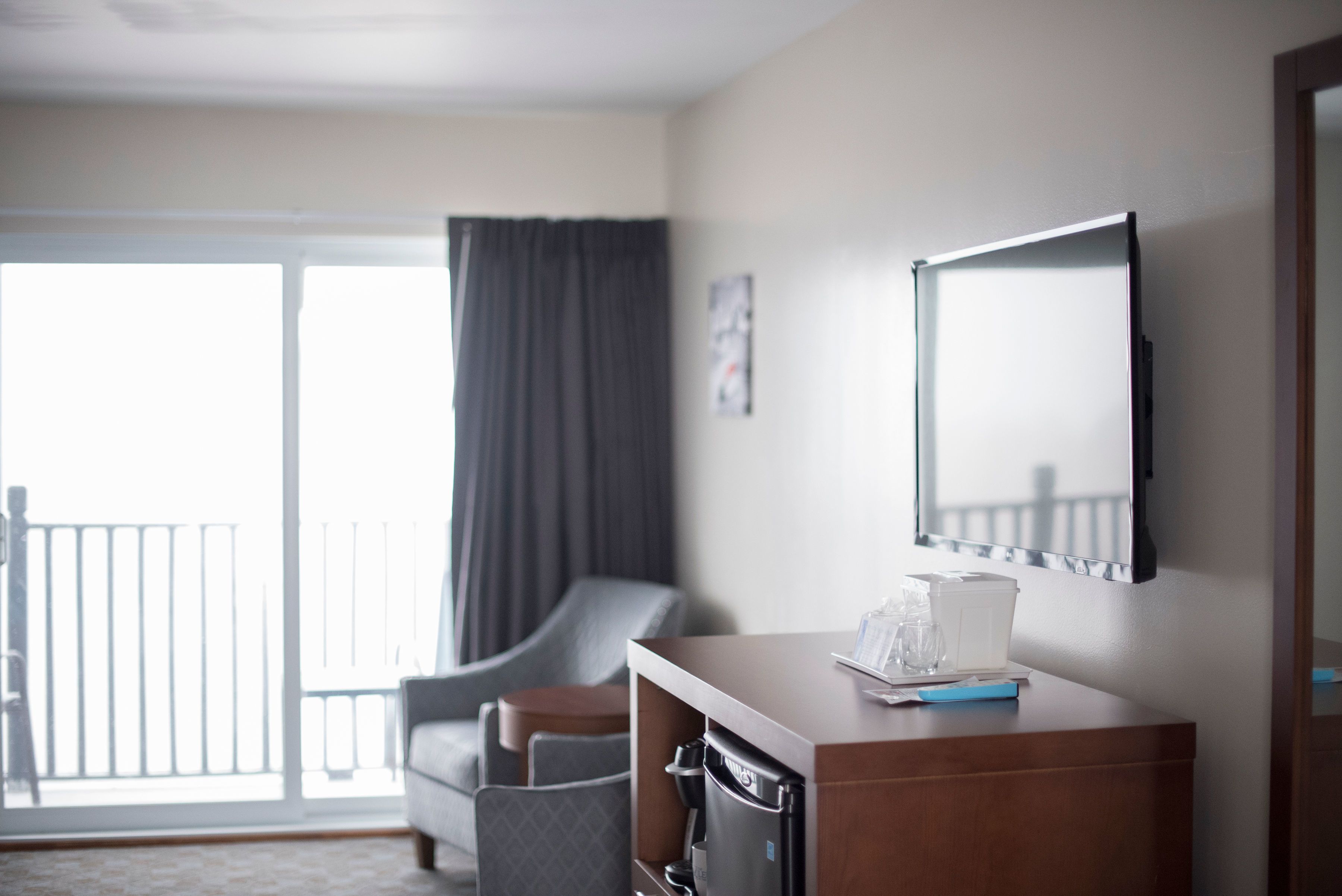 A hotel room with a sofa, a coffee machine, a small table with a glass, and a large window with a view of a balcony.