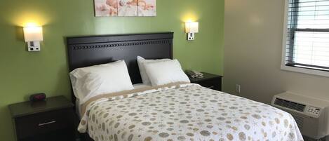 A hotel room with a bed, two bedside tables, a nightstand, a wall-mounted lamp, a wall art depicting sea creatures, and a window with blinds.