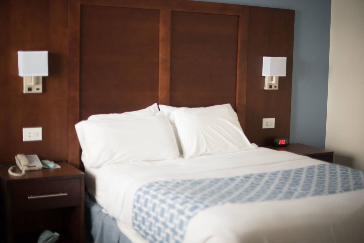A hotel room with a large bed, two bedside tables, a nightstand, a phone, and a clock.