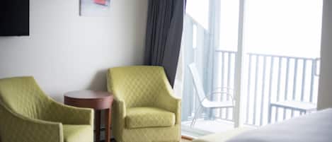A hotel room with a bed, two armchairs, a small table, a painting on the wall, and a balcony with a railing.