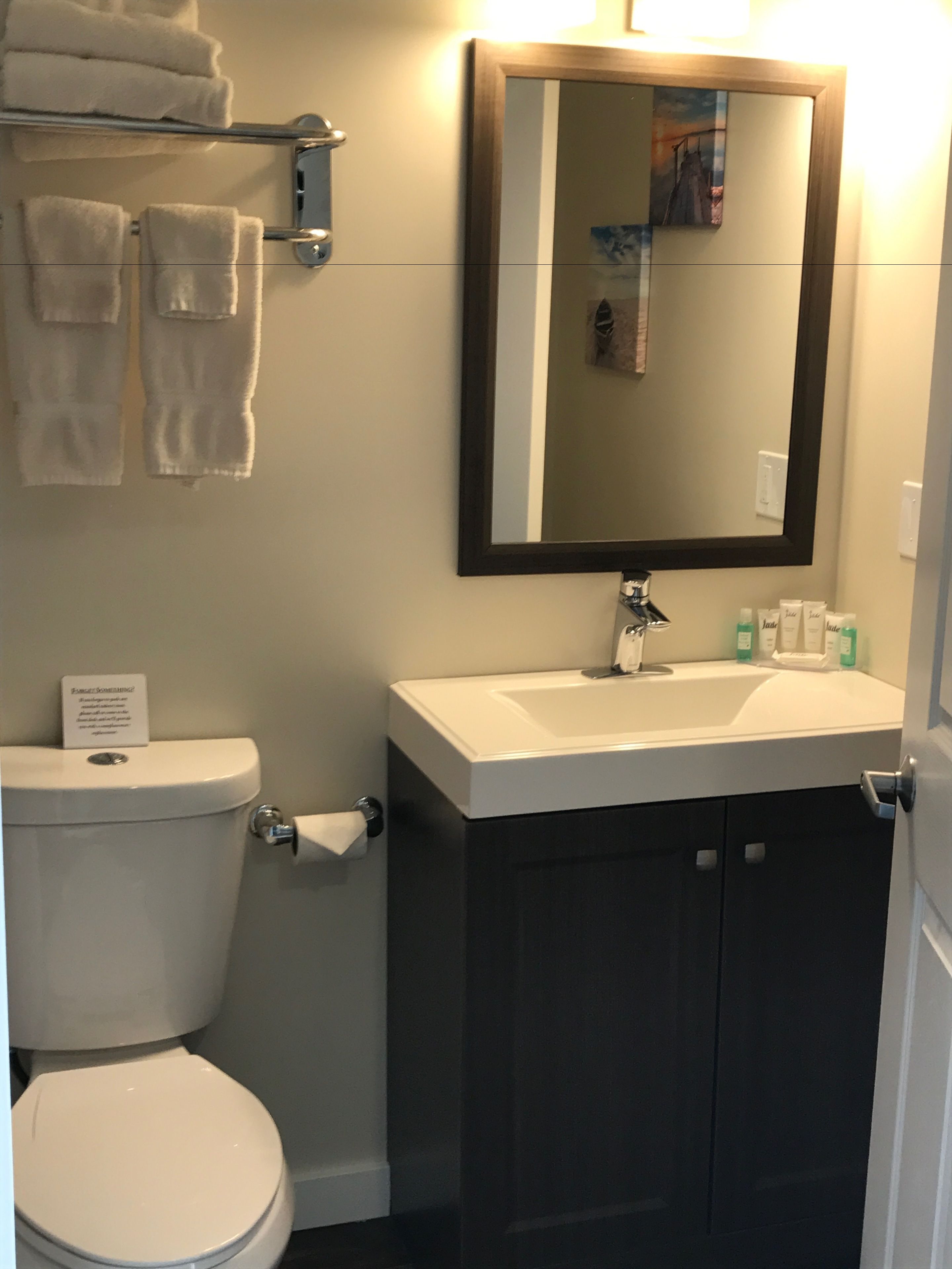 A bathroom with a toilet, sink, mirror, and towel rack.
