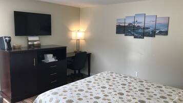 A hotel room with a bed, a desk, a dresser, a television, and a wall with three paintings.