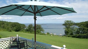 Une terrasse avec une table et des chaises, donnant sur une étendue d’eau et une zone herbeuse agrémentée de parasols.
