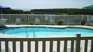 Une piscine entourée d’une clôture blanche, avec des chaises longues et des parasols.