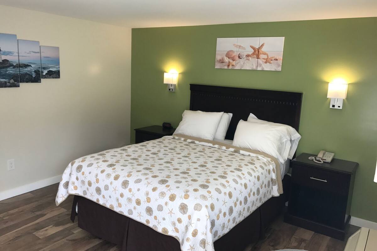 A neatly made bed with a patterned bedspread, two bedside tables with lamps, and a wall-mounted artwork depicting a beach scene.