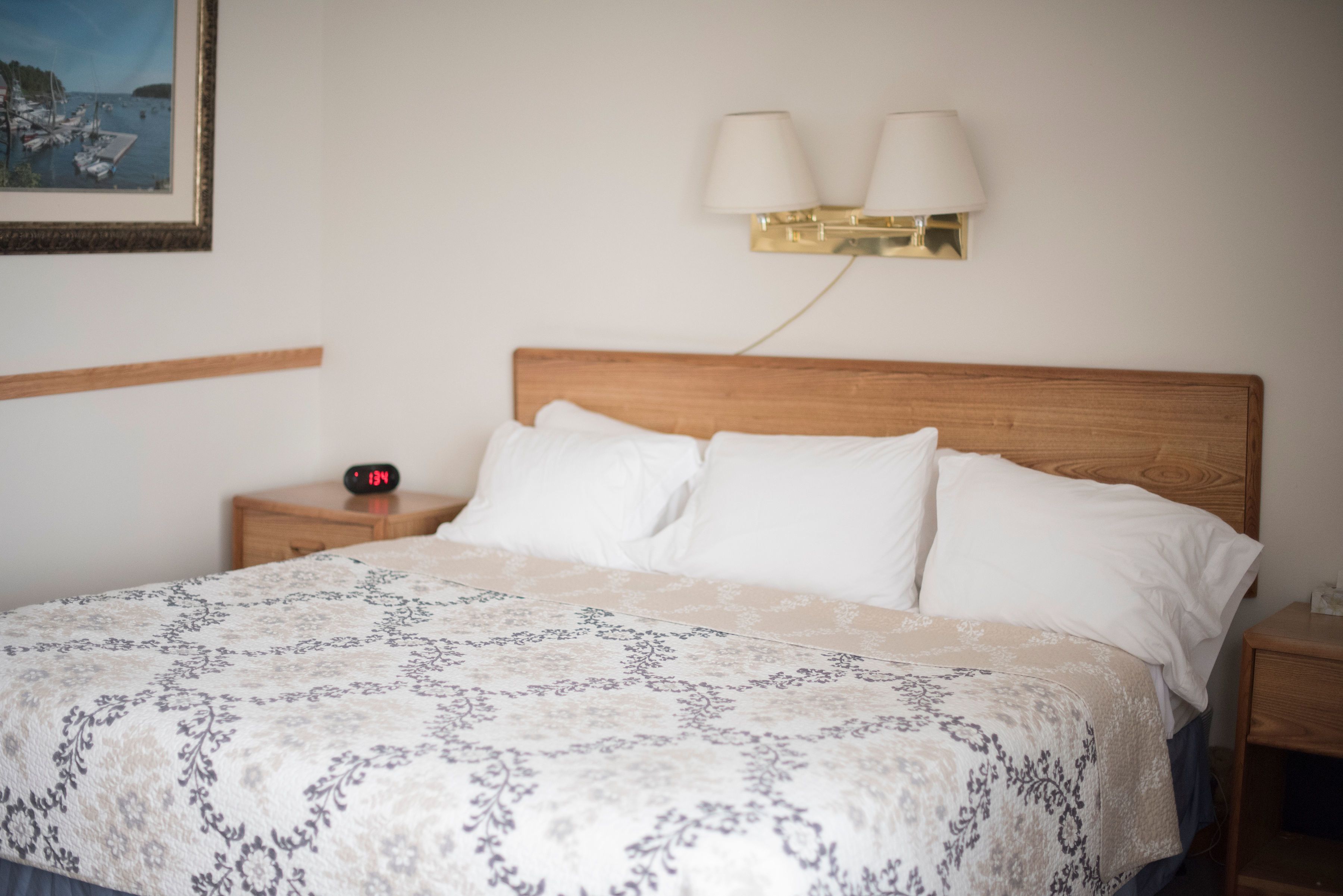 A neatly made bed with a patterned bedspread, a wooden headboard, and a bedside table with a clock.