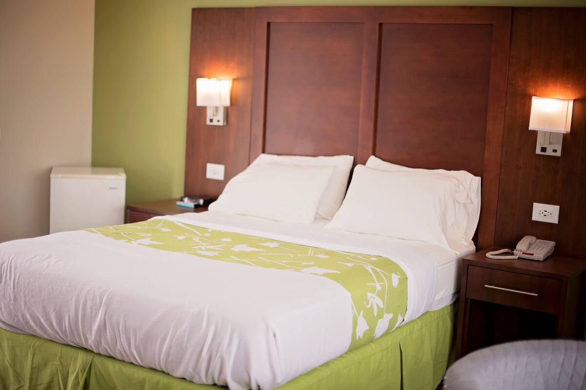 A hotel room with a bed, bedside tables, a telephone, and a wall-mounted light fixture.
