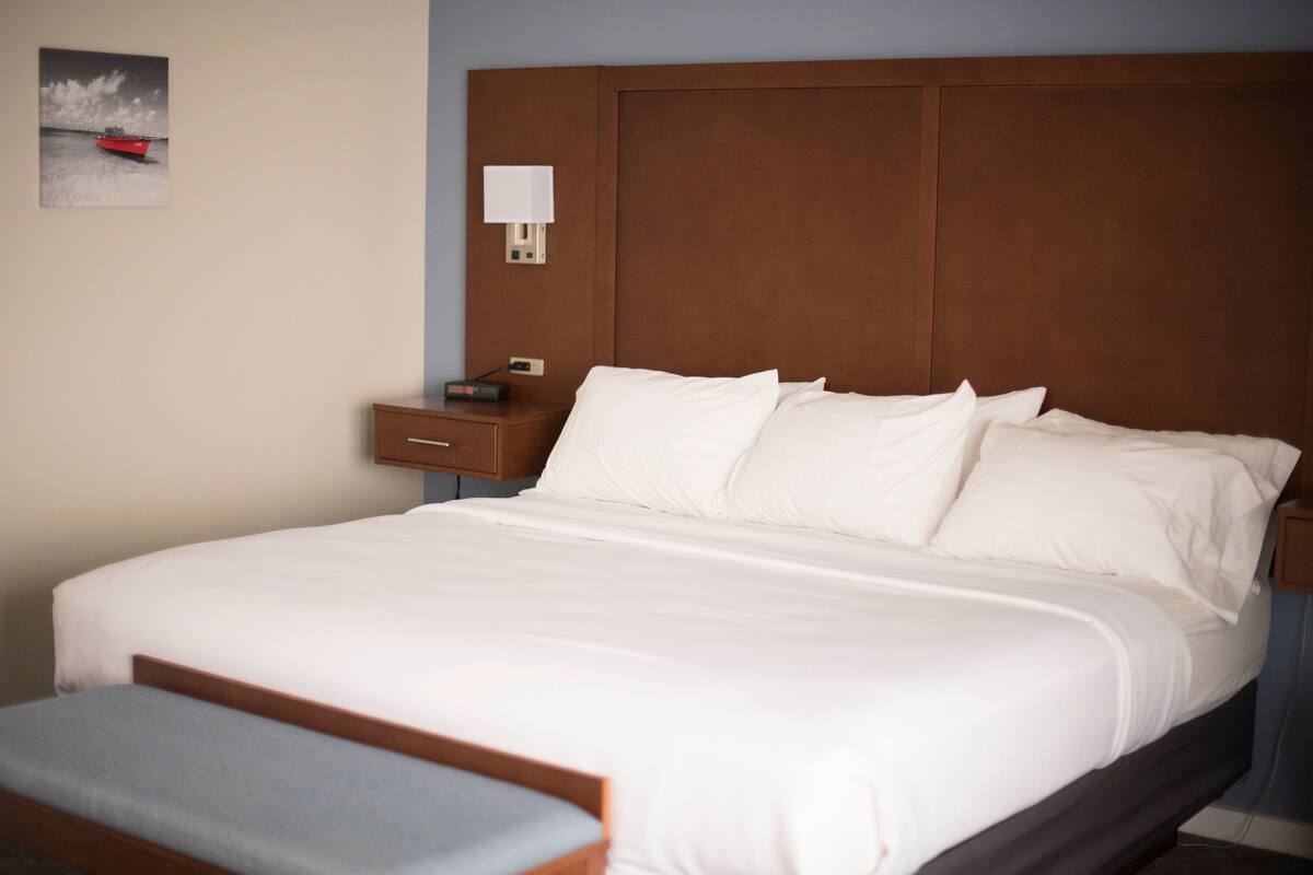 A neatly made bed with white linens, a wooden headboard, and a nightstand with a lamp.