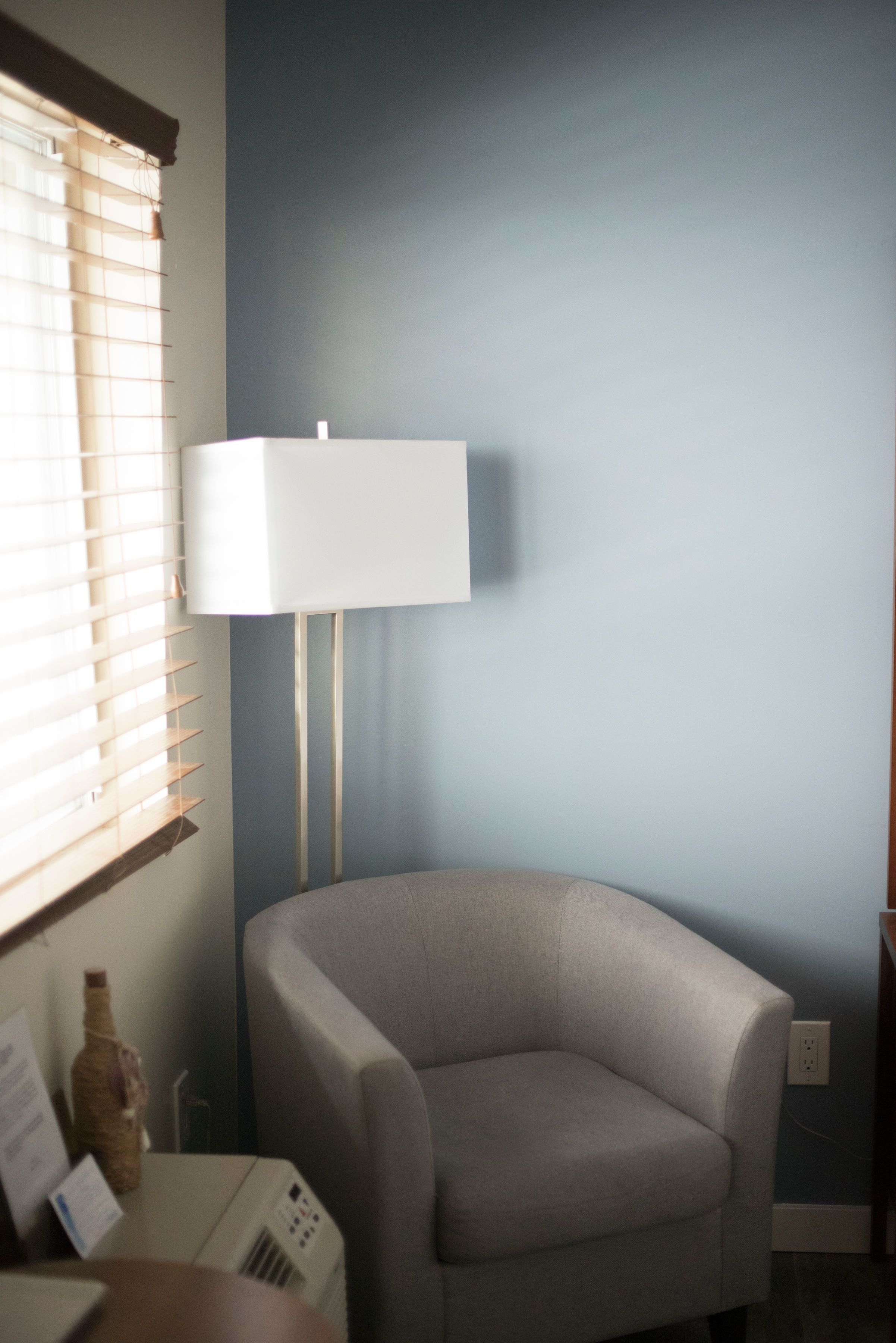A room with a blue wall, a white lamp, and a grey armchair.