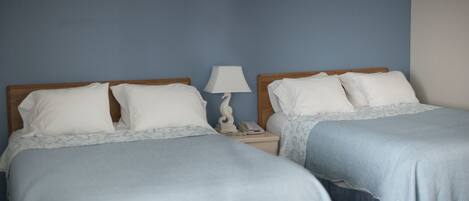Dos camas individuales con cabeceros de madera, ropa de cama blanca y una mesita de noche con lámpara.