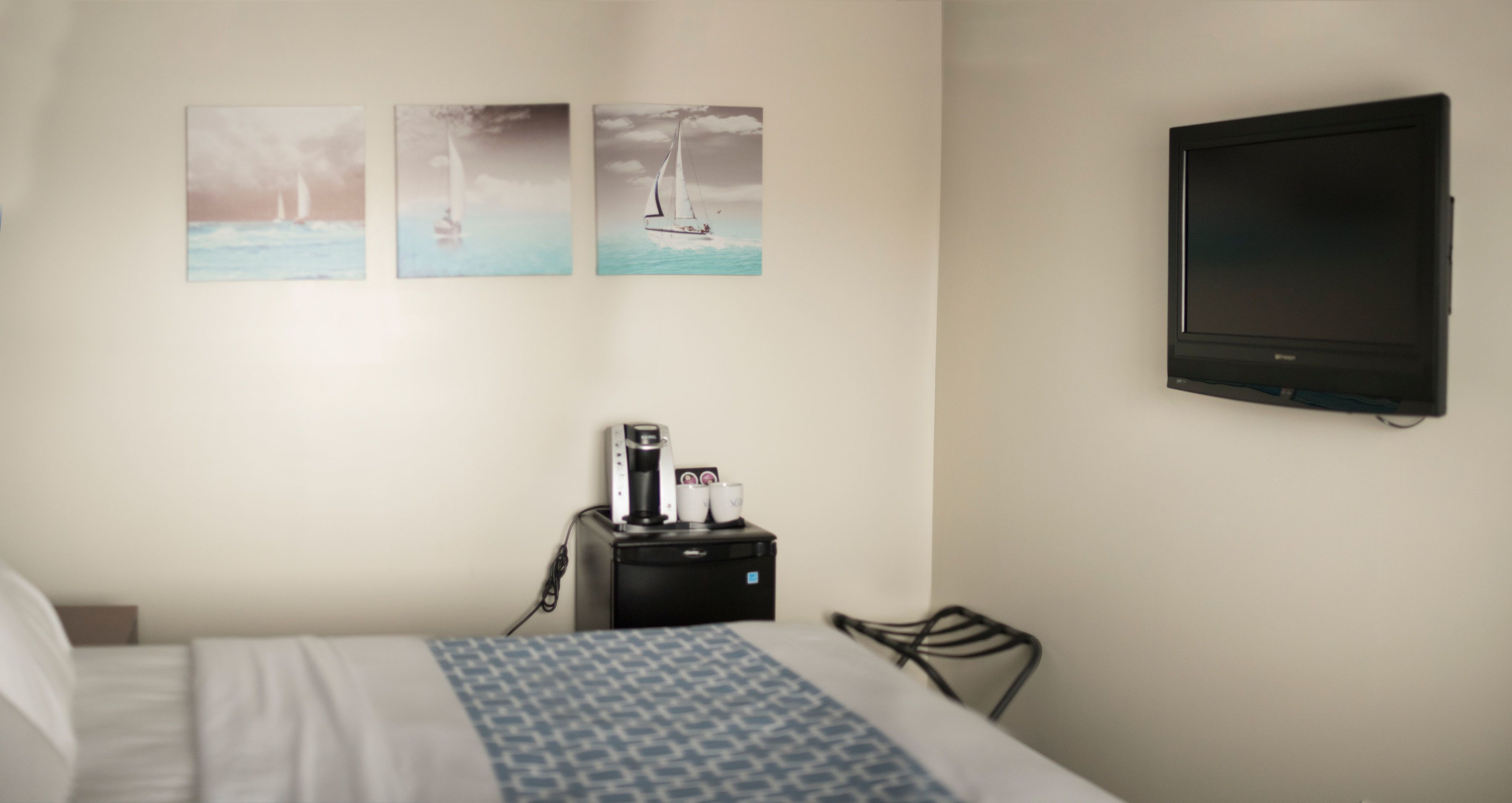 A hotel room with a bed, a coffee maker, a TV, and three paintings on the wall.