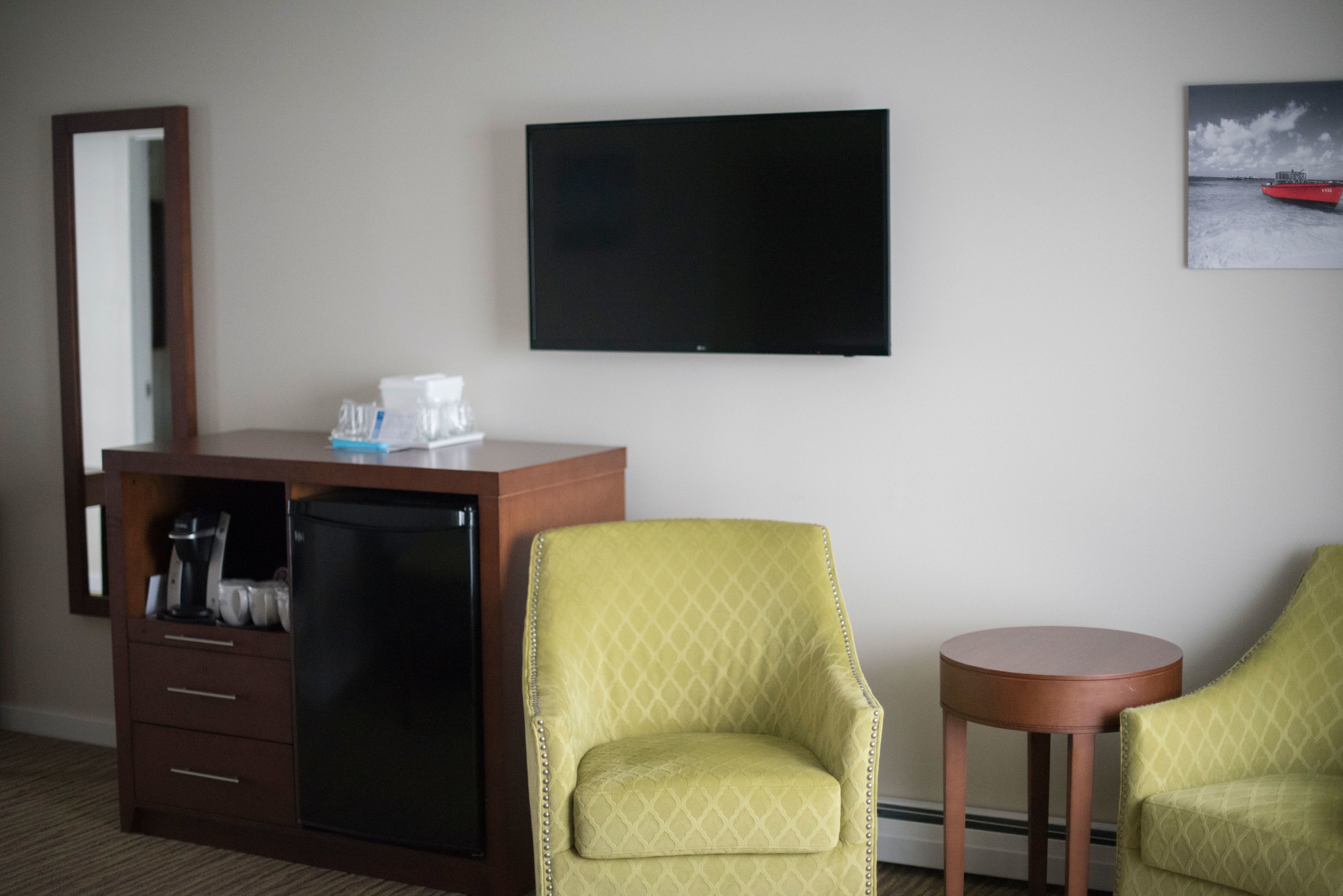 A hotel room with a minibar, a flat-screen TV, two armchairs, and a small table.