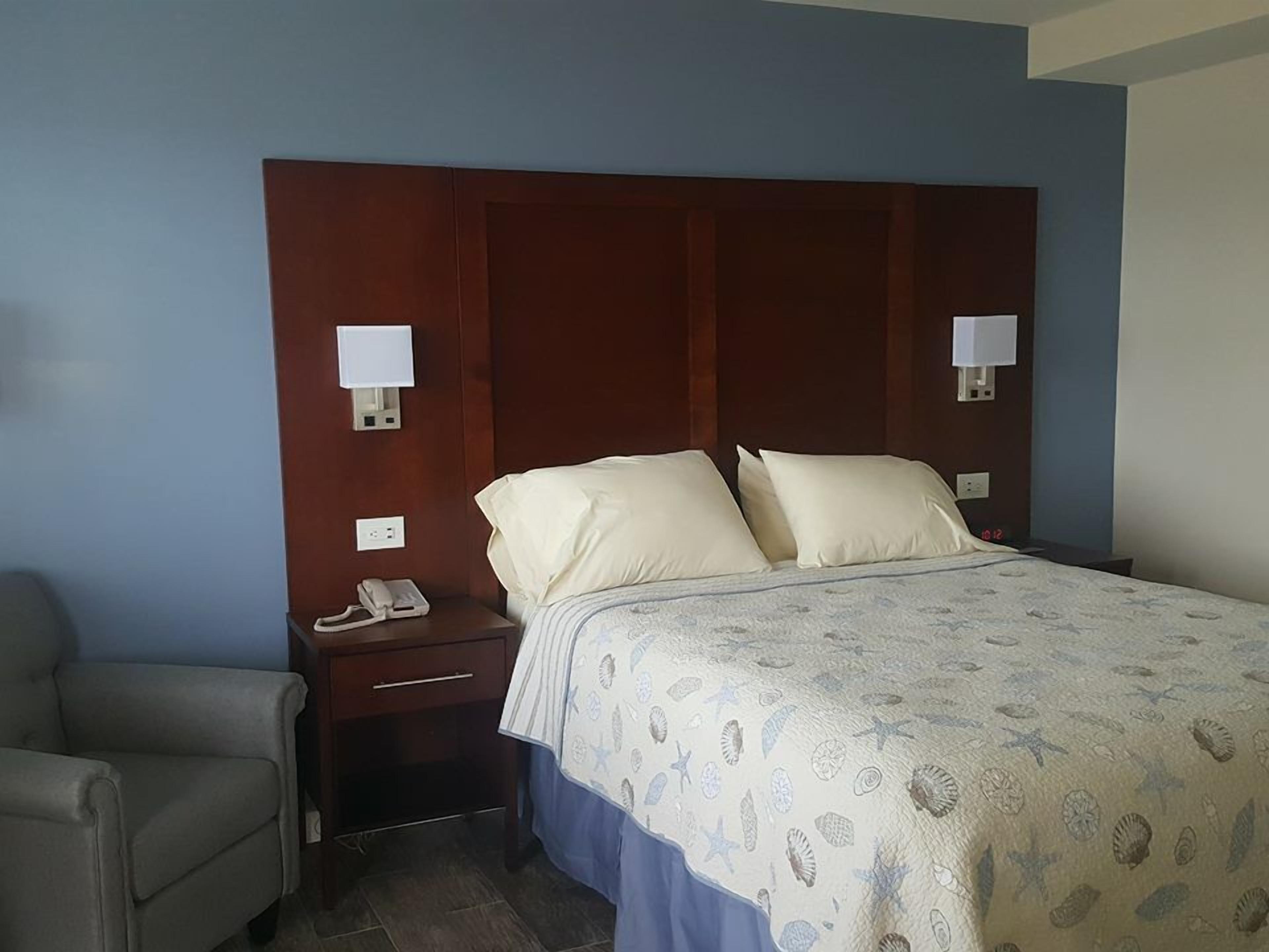 Habitación de hotel con cama, mesitas de noche, teléfono y una silla.