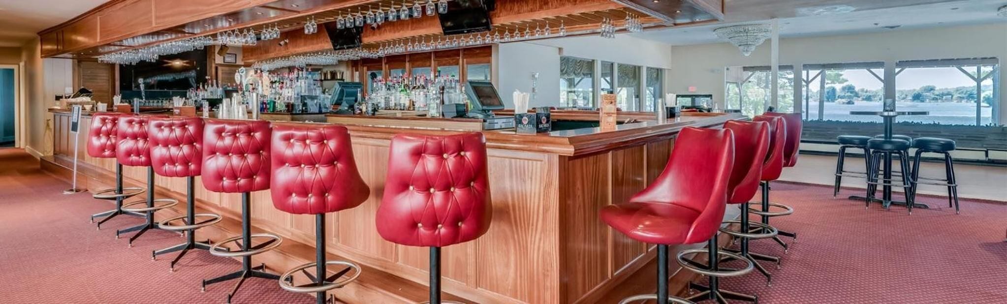 A bar area with red bar stools and a wooden counter, equipped with a TV and various bottles.
