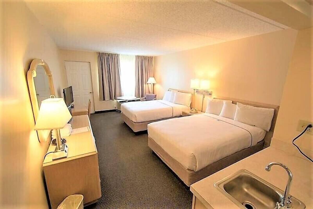 Een hotelkamer met twee bedden, een bureau met lamp, een televisie en een wastafel.